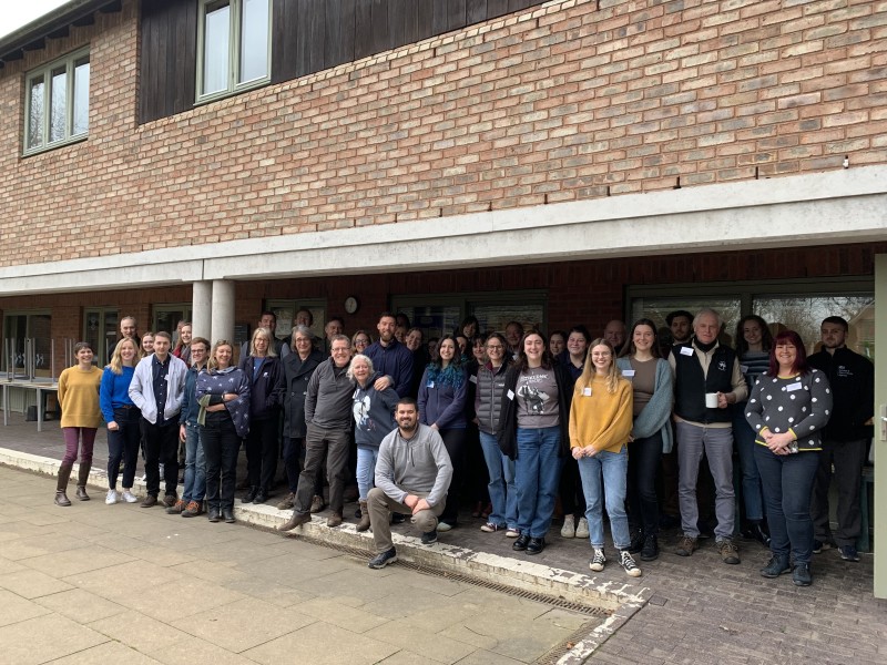 A large group of people standing in front of a brick building smiling at the camera 