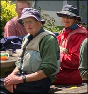 A man and woman sat at a picnic table in outdoor clothing